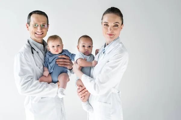 Pediatras segurando bebês pequenos e olhando para câmera isolada em branco — Fotografia de Stock