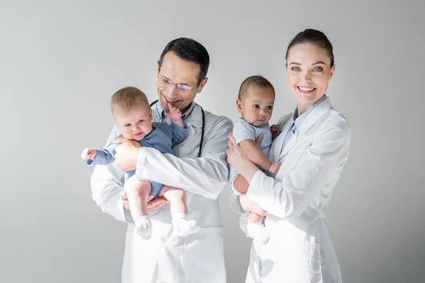 Pediatras adultos felizes segurando bebês pequenos isolados em cinza — Fotografia de Stock