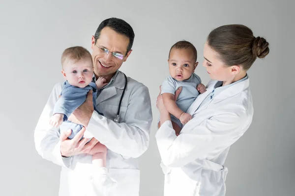 Pediatras felizes segurando pequenos bebês isolados em cinza — Fotografia de Stock