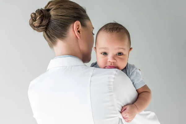 Visão traseira do pediatra feminino com bebê afro-americano isolado em cinza — Fotografia de Stock