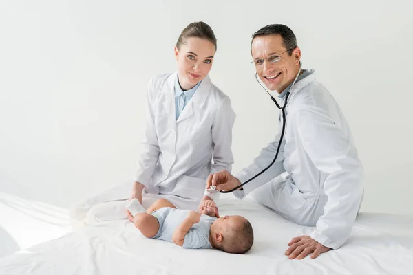 Pediatras felizes ouvindo respiração de bebê pequeno com estetoscópio — Fotografia de Stock