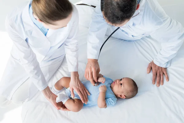 Vista ad alto angolo dei pediatri che ascoltano il respiro del piccolo bambino con stetoscopio — Foto stock