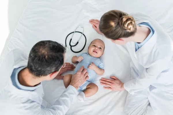 Visão de alto ângulo de pediatras cócegas pequeno bebê na cama — Fotografia de Stock