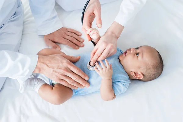 Inyección recortada de pediatras escuchando latidos del corazón de un bebé pequeño con estetoscopio - foto de stock