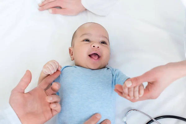 Cropped shot of pediatricians taking care of adorable little baby on bed — Stock Photo