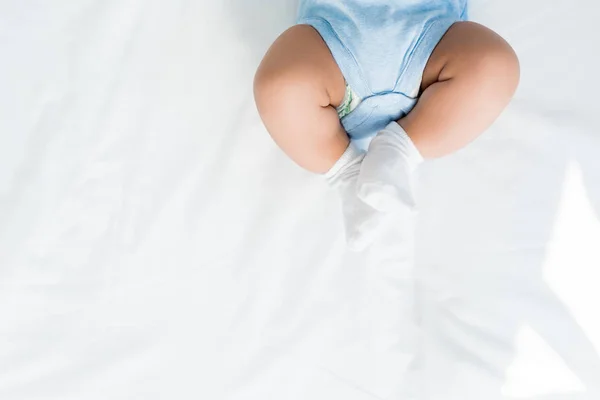 Cropped shot of little child in rompers and white socks lying on bed — Stock Photo