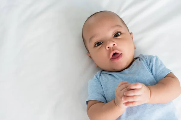 Säugling mit überraschtem Gesichtsausdruck, der im Bett in die Kamera blickt — Stockfoto