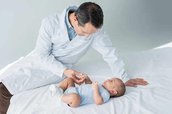 Pediatra adulto seduto sul letto con bambino piccolo — Foto stock