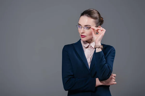Красива доросла бізнес-леді в стильному костюмі і окулярах дивиться ізольовано на сірому — стокове фото