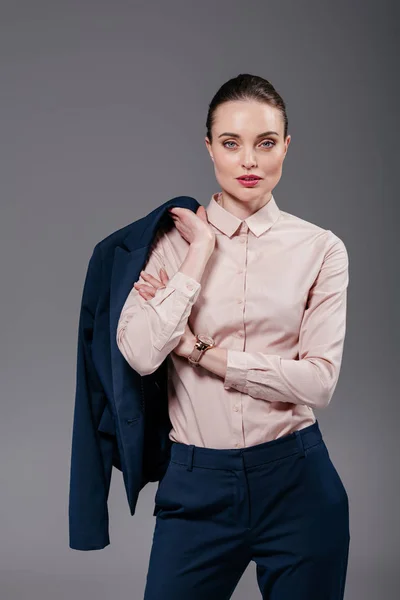 Stilvolle erwachsene Geschäftsfrau mit Jacke auf der Schulter, die in die Kamera schaut, isoliert auf grau — Stockfoto