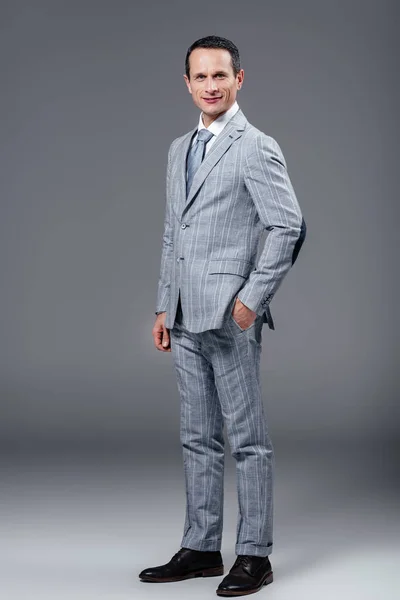 Дорослий бізнесмен у стильному костюмі дивиться на камеру на сірому — стокове фото