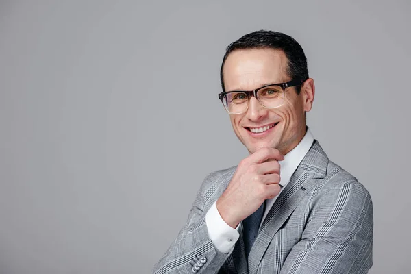 Smiling adult businessman with hand on chin isolated on grey — Stock Photo