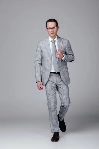 Elegante uomo d'affari adulto in abito grigio che cammina davanti alla macchina fotografica su grigio — Foto stock