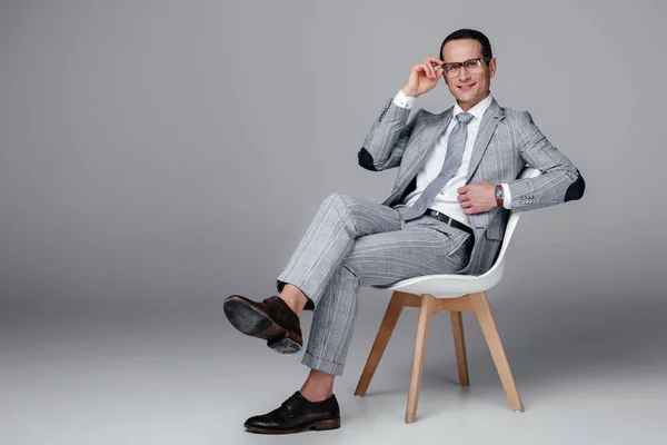 Sonriente adulto hombre de negocios en elegante traje sentado en la silla en gris - foto de stock