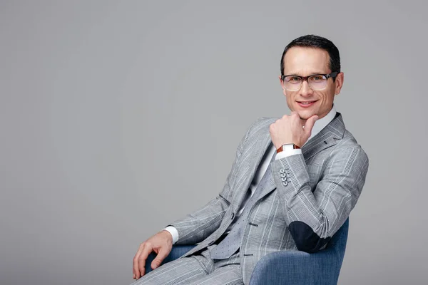 Retrato de primer plano del hombre de negocios adulto en traje elegante sentado en silla con la mano en la barbilla aislado en gris - foto de stock