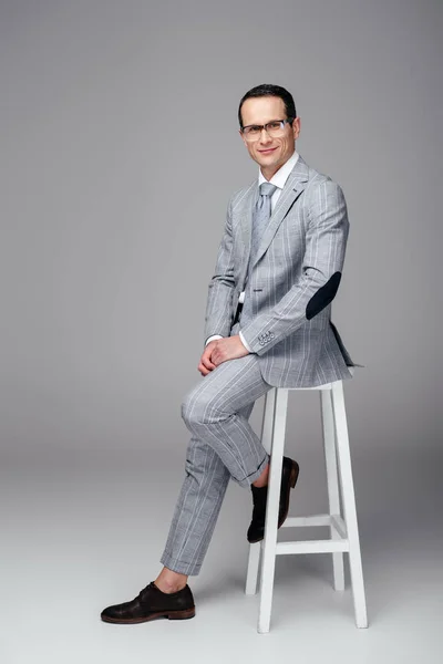 Handsome adult businessman in stylish suit sitting on chair on grey — Stock Photo