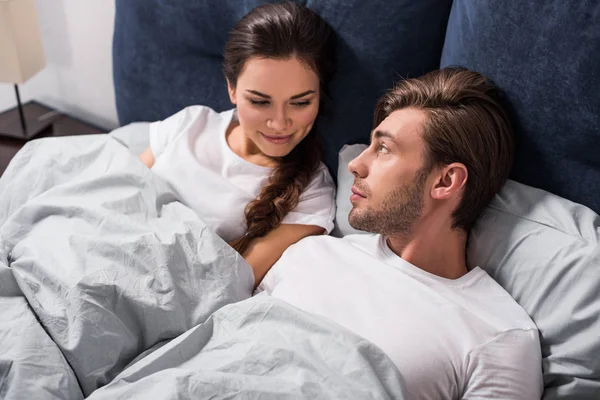 Hombre y mujer sonrientes acostados en la cama por la mañana - foto de stock
