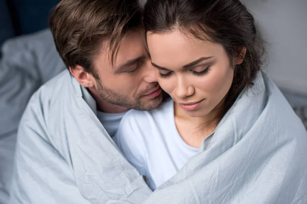 Young man and woman tenderly embracing under blanket — Stock Photo