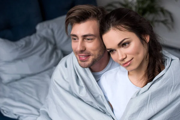 Beautiful couple tenderly embracing under blanket — Stock Photo