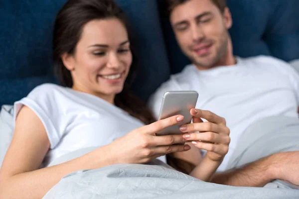 Mulher usando smartphone enquanto deitada na cama com o marido — Fotografia de Stock