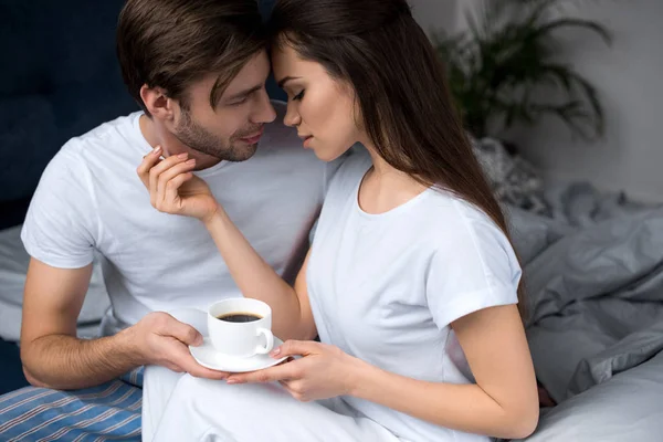 Mulher segurando xícara de café e abraçando seu marido enquanto na cama — Fotografia de Stock