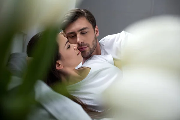Mulher abraçando e olhando para o marido enquanto deitada na cama — Fotografia de Stock