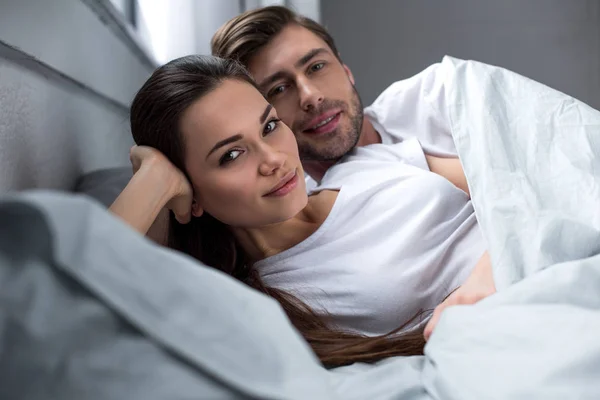 Jeune couple attrayant étreignant tout couché au lit — Photo de stock