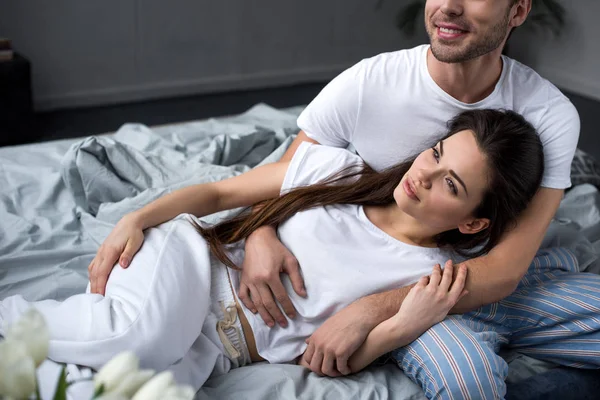 Sonriente pareja tiernamente abrazándose mientras está acostado en la cama - foto de stock