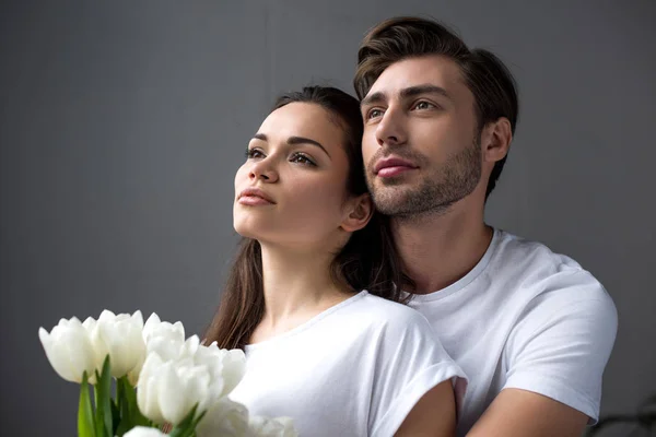 Romantisches Paar mit Tulpen, die sich im Schlafzimmer zärtlich umarmen — Stockfoto