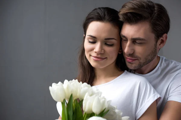 Barbudo hombre abrazando atractiva morena esposa con ramo de tulipanes - foto de stock