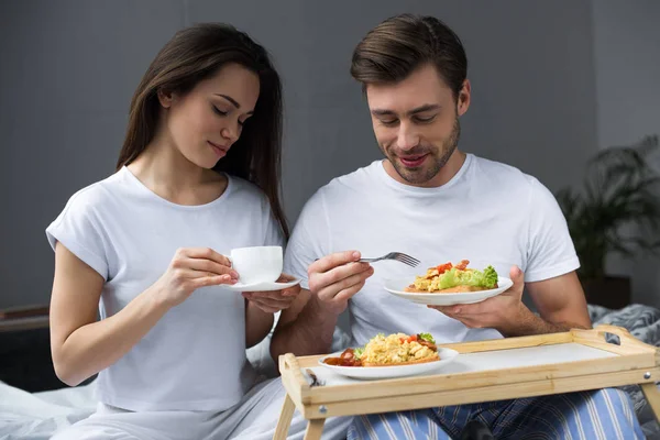 Lächelnde Frau und Mann trinken Kaffee und frühstücken im Bett — Stockfoto