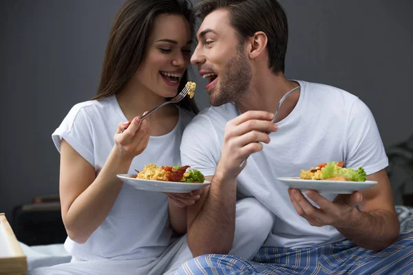 Atractiva pareja comiendo huevos revueltos en la cama - foto de stock