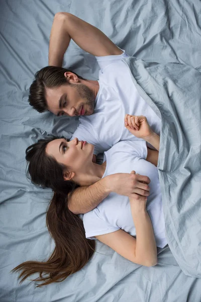 Усміхнений чоловік і жінка ніжно обіймаються, лежачи в ліжку — стокове фото