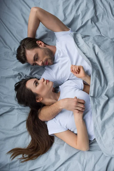 Smiling man and woman tenderly embracing while lying in bed — Stock Photo