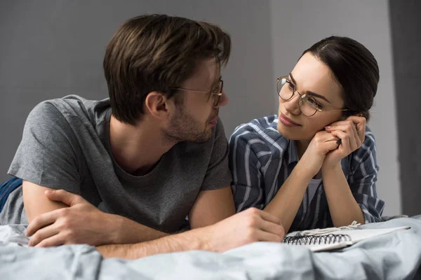 Junges Paar mit Notizblock im Bett liegend und einander anschauend — Stockfoto
