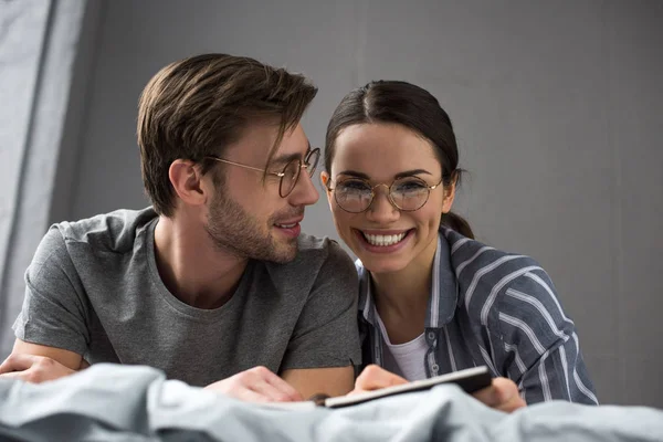 Happy man and woman writing in notepad while lying in bed — Stock Photo