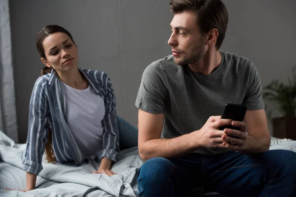 Frau sieht ihren Mann misstrauisch mit Smartphone an — Stockfoto