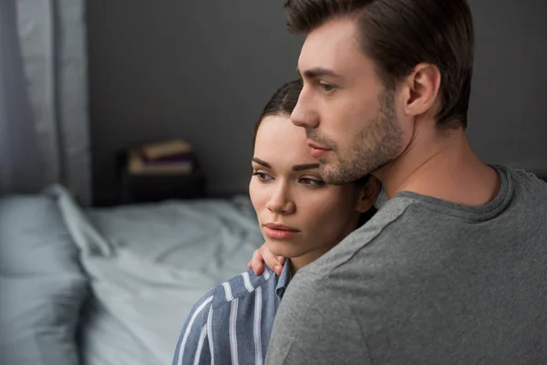 Junges attraktives Paar umarmt sich im Schlafzimmer und schaut weg — Stockfoto
