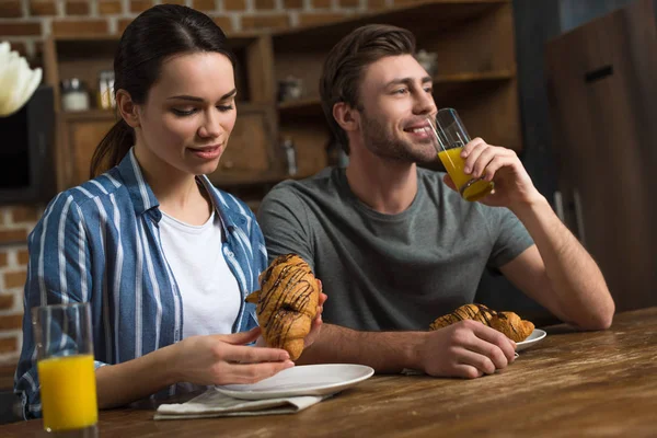 Paar trinkt Saft und isst Croissants am Küchentisch — Stockfoto