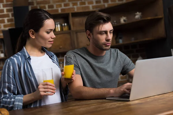 Жена предлагает сок своему мужу, работающему за ноутбуком — стоковое фото