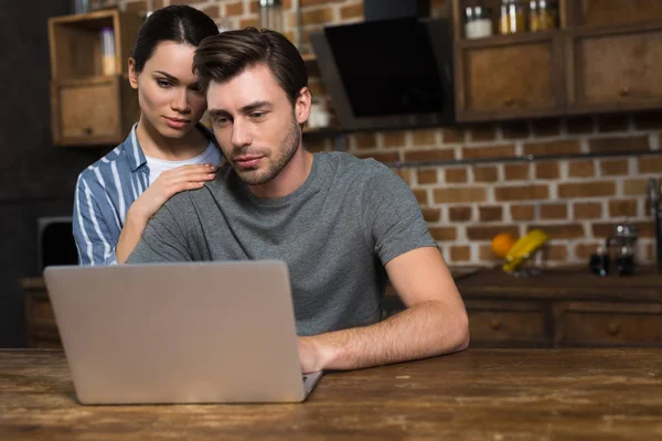 Giovane coppia guardando lo schermo del computer portatile sul tavolo della cucina — Foto stock