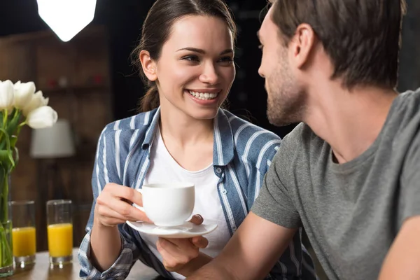 Mulher bonita bebendo café e sorrindo para o marido na cozinha — Fotografia de Stock