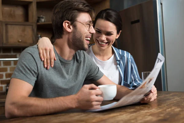 Happy couple enjoying breakfast with coffee and newspaper on kitchen — Stock Photo