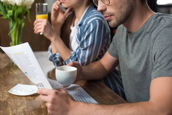 Jovem mulher bebendo suco falando ao telefone enquanto o homem bebendo café e ler jornal — Fotografia de Stock