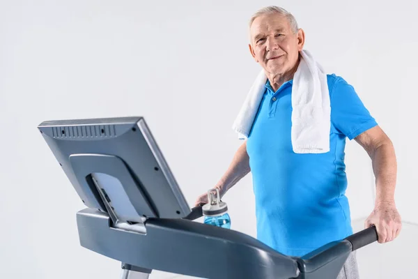 Side view of senior man with towel exercising on treadmill isolated on grey — Stock Photo