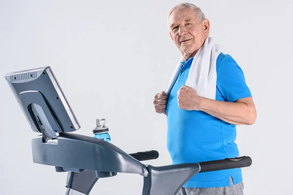 Side view of smiling senior man with towel exercising on treadmill isolated on grey — Stock Photo