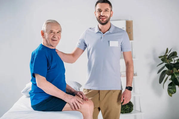 Porträt des Reha-Therapeuten und lächelnden Seniors auf Massagetisch — Stockfoto