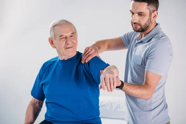 Retrato de fisioterapeuta haciendo masaje a hombre mayor sonriente en mesa de masaje - foto de stock