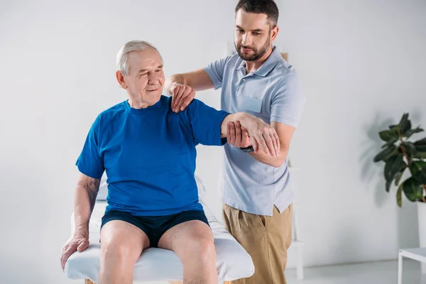 Terapeuta de rehabilitación de retratos haciendo masaje al hombre mayor en la mesa de masaje - foto de stock