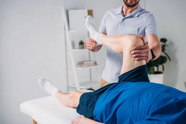 Vue partielle du thérapeute de réadaptation massant les jambes des personnes âgées sur la table de massage — Photo de stock